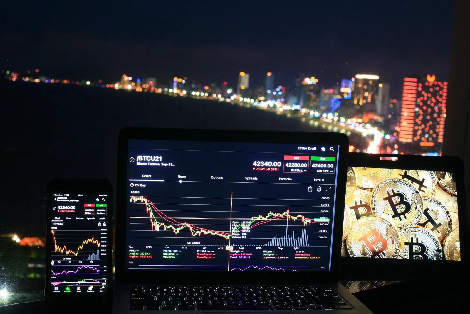 Ordinateur portable et téléphone affichant des graphiques de trading crypto devant une ville la nuit